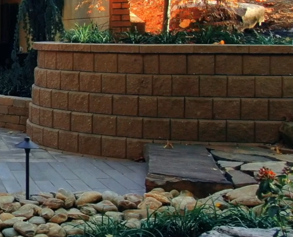 Retaining wall on a patio supporting a beautifully landscaped bed with vibrant plants, showcasing durability and elegance in hardscaping design.