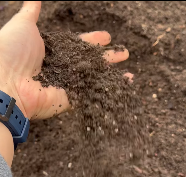 Premium compost being turned over by a hand showing the even consistency of the organic material.